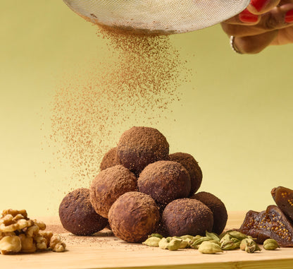 On a light background, a pile of round fig and date truffles coated with chocolate.